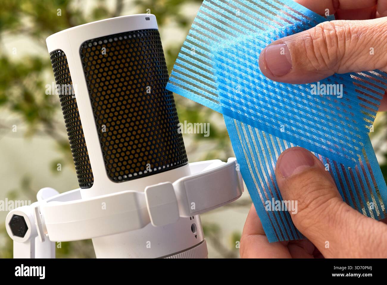 Mains manipulant des couches de maille en plastique bleu près d'un microphone à condensateur blanc pour enregistrer les rayures et les déclenchements audio ASMR texturés. Banque D'Images