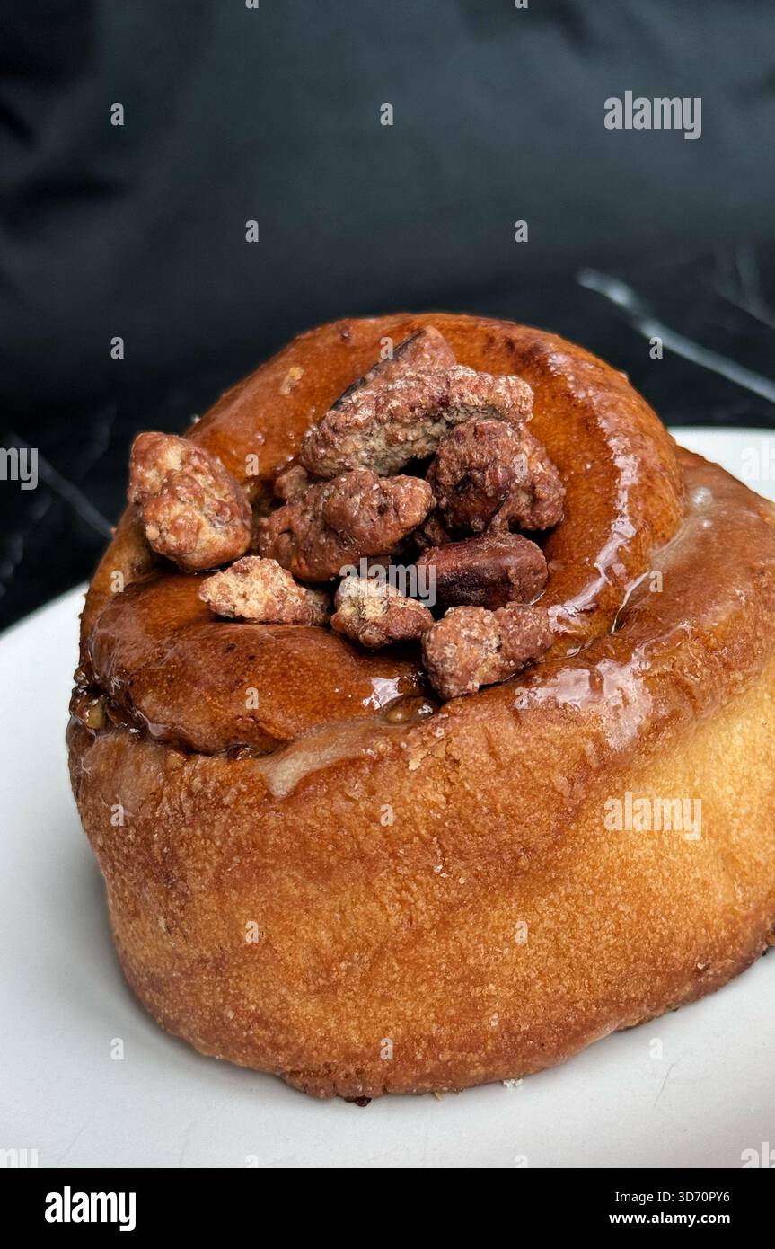 Gros plan d'un rouleau de cannelle glacé surmonté de noix confites sur une plaque blanche sur un fond sombre - Image de stock capturée avec un smartphone