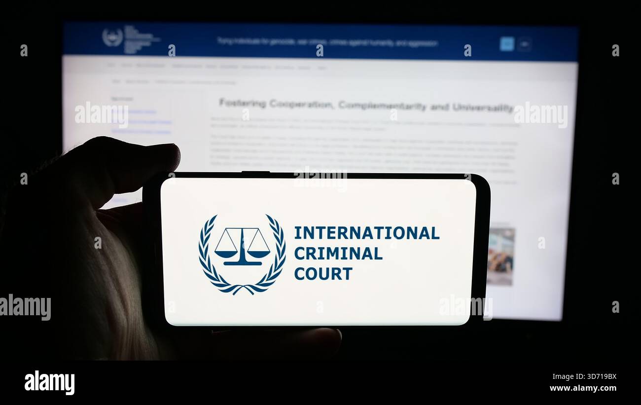 Dans cette illustration photo, une personne tient un téléphone portable avec le logo de l'organisation Cour pénale internationale (CPI) sur l'écran devant la page Web. Banque D'Images