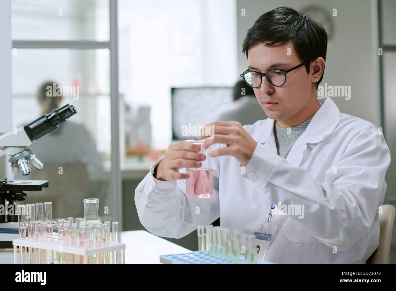 Jeune homme adulte conduisant une expérience chimique dans un laboratoire médical Banque D'Images