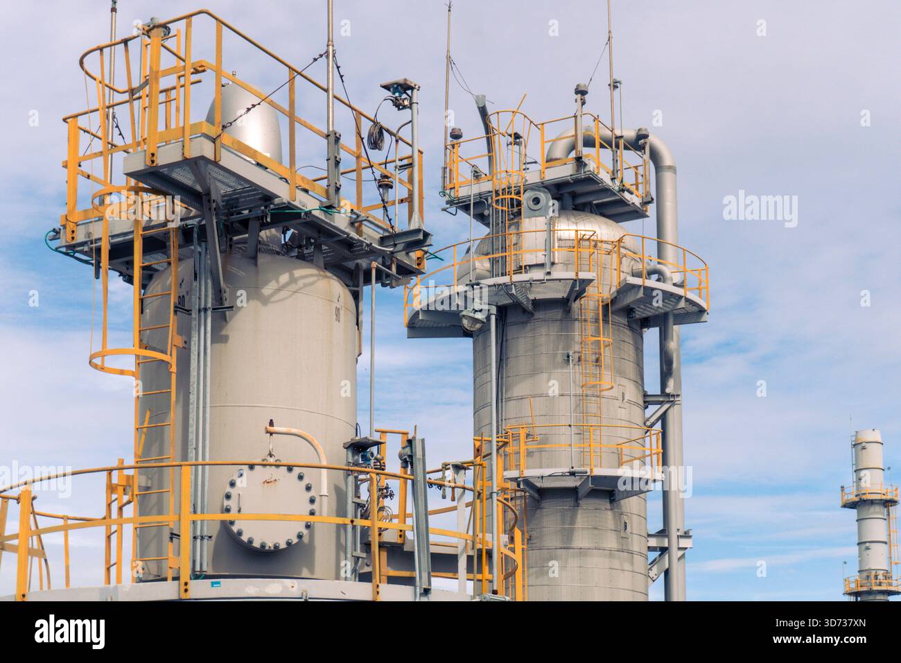 Une vue rapprochée des tours de traitement de raffinerie avec des plates-formes métalliques, des échelles, des systèmes de tuyauterie et des rampes de sécurité industrielle sous un ciel lumineux. Banque D'Images