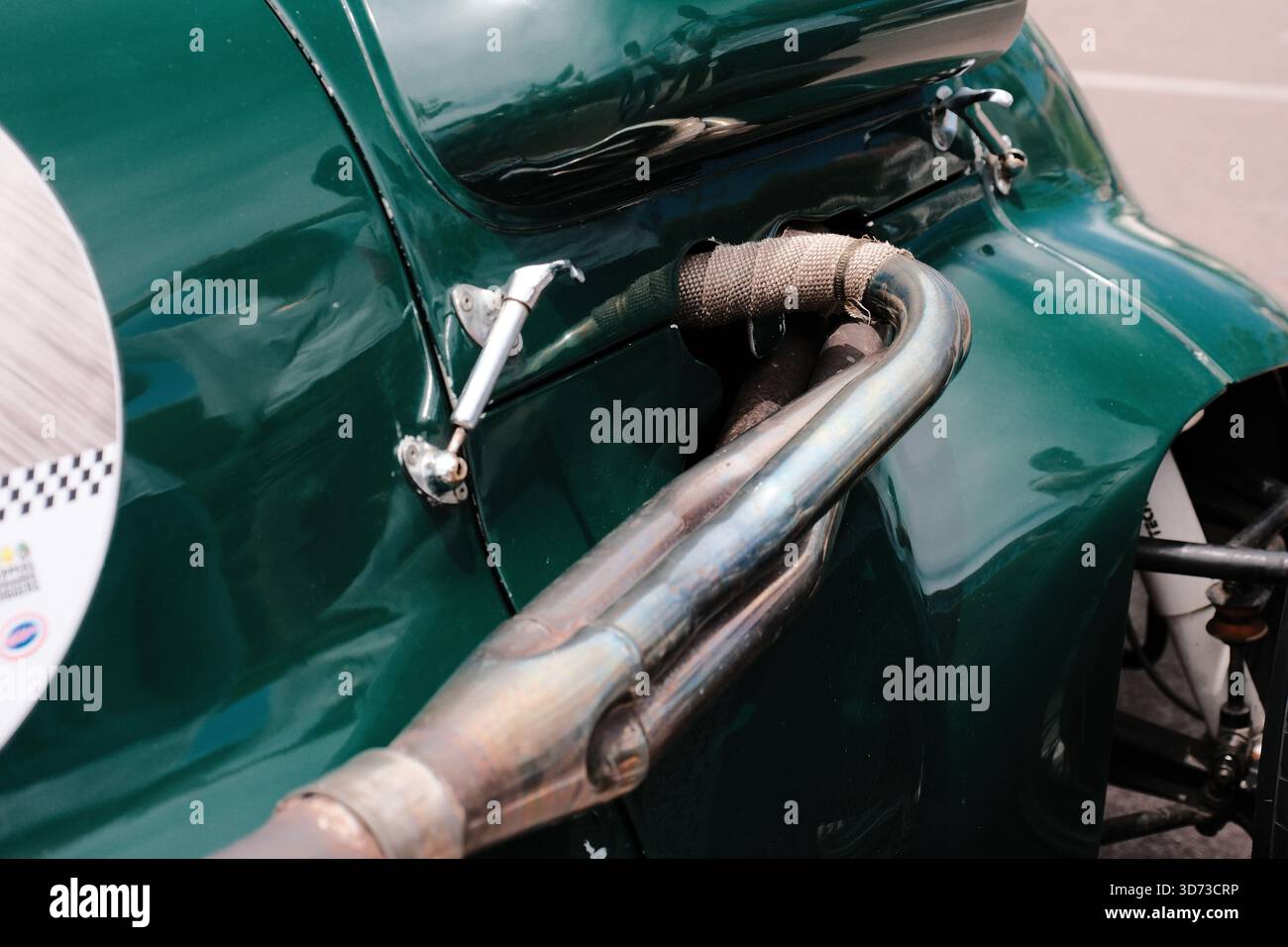 Gros plan d'une voiture de course verte d'époque montrant ses tuyaux d'échappement exposés, son collecteur enveloppé de chaleur et sa quincaillerie de panneau de carrosserie rétro. Banque D'Images