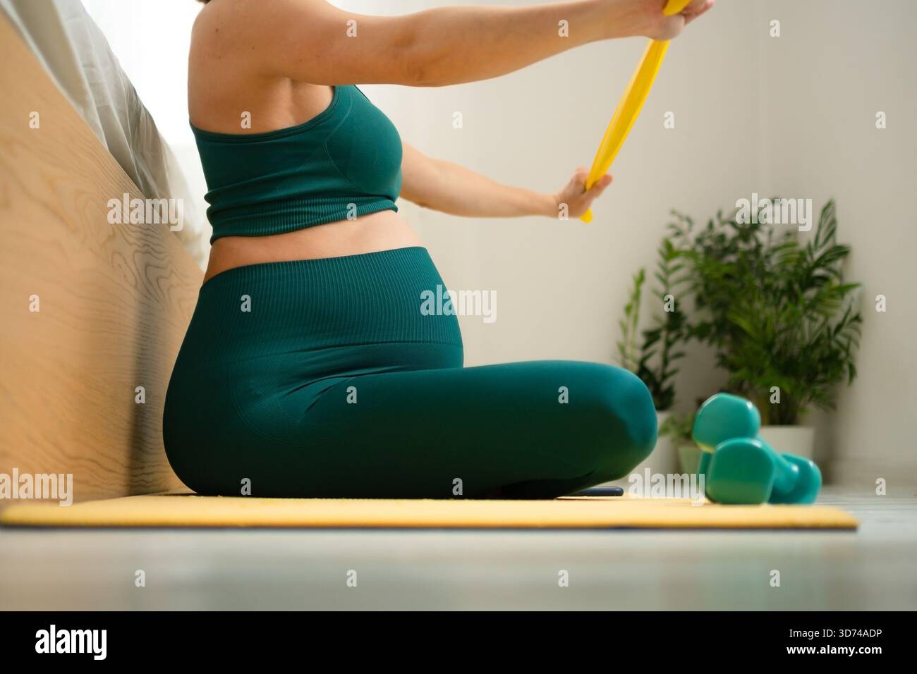 Femme enceinte sereine dans la posture étirée des jambes croisées sur le lit, maintenant la routine de forme physique. Nourrir le corps et l'esprit en attendant l'arrivée de bébé. Banque D'Images