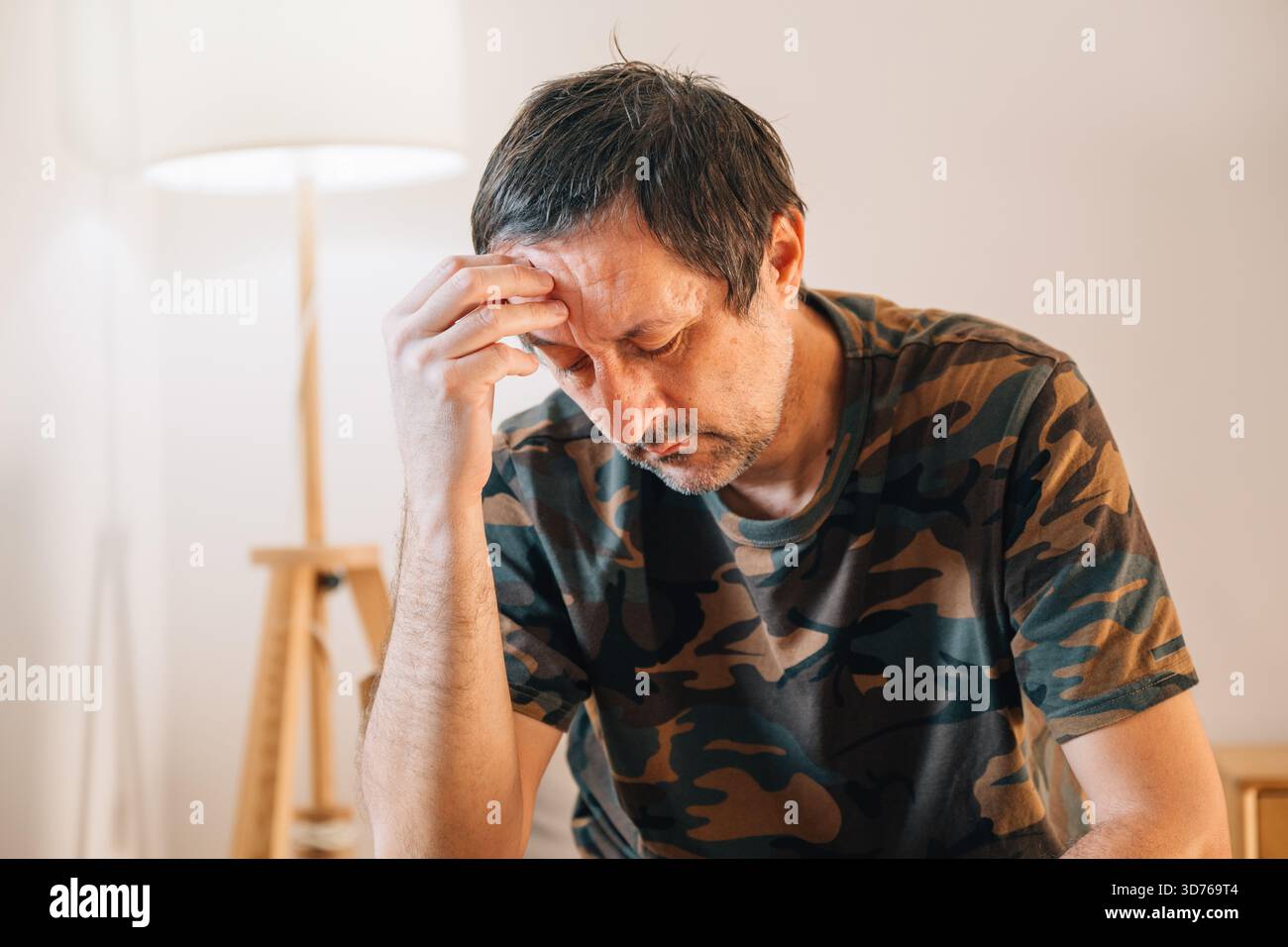 Homme d'âge moyen stressé assis sur une chaise à la maison, la tête dans les mains, submergé par l'émotion dans une lumière naturelle chaude près de la fenêtre. Mise au point sélective. Banque D'Images