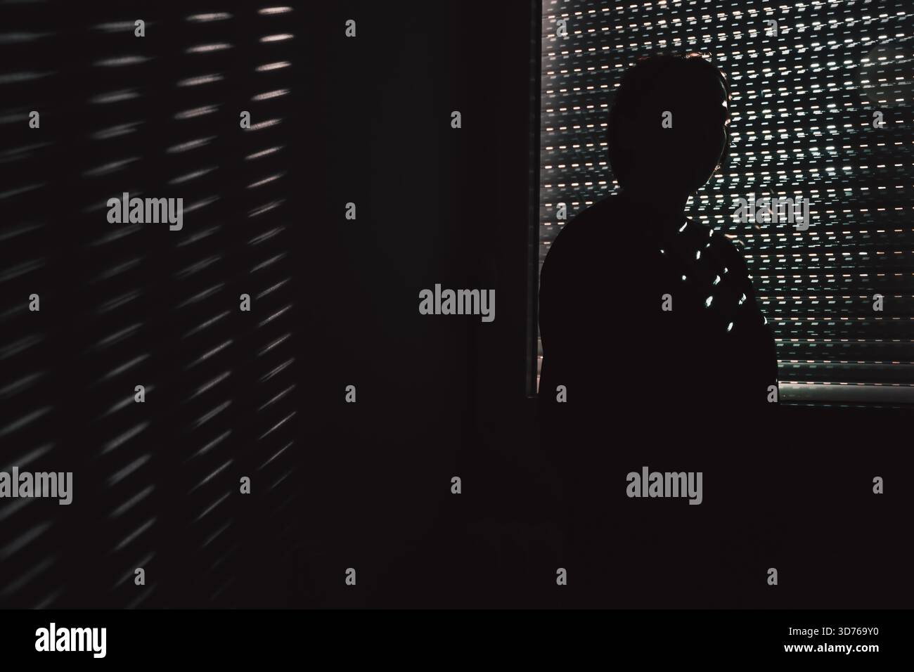 Silhouette d'une femme dans une pièce sombre touchant son front près de stores fermés, lumière à motifs dramatiques symbolisant la tension émotionnelle, la solitude et le Dee Banque D'Images