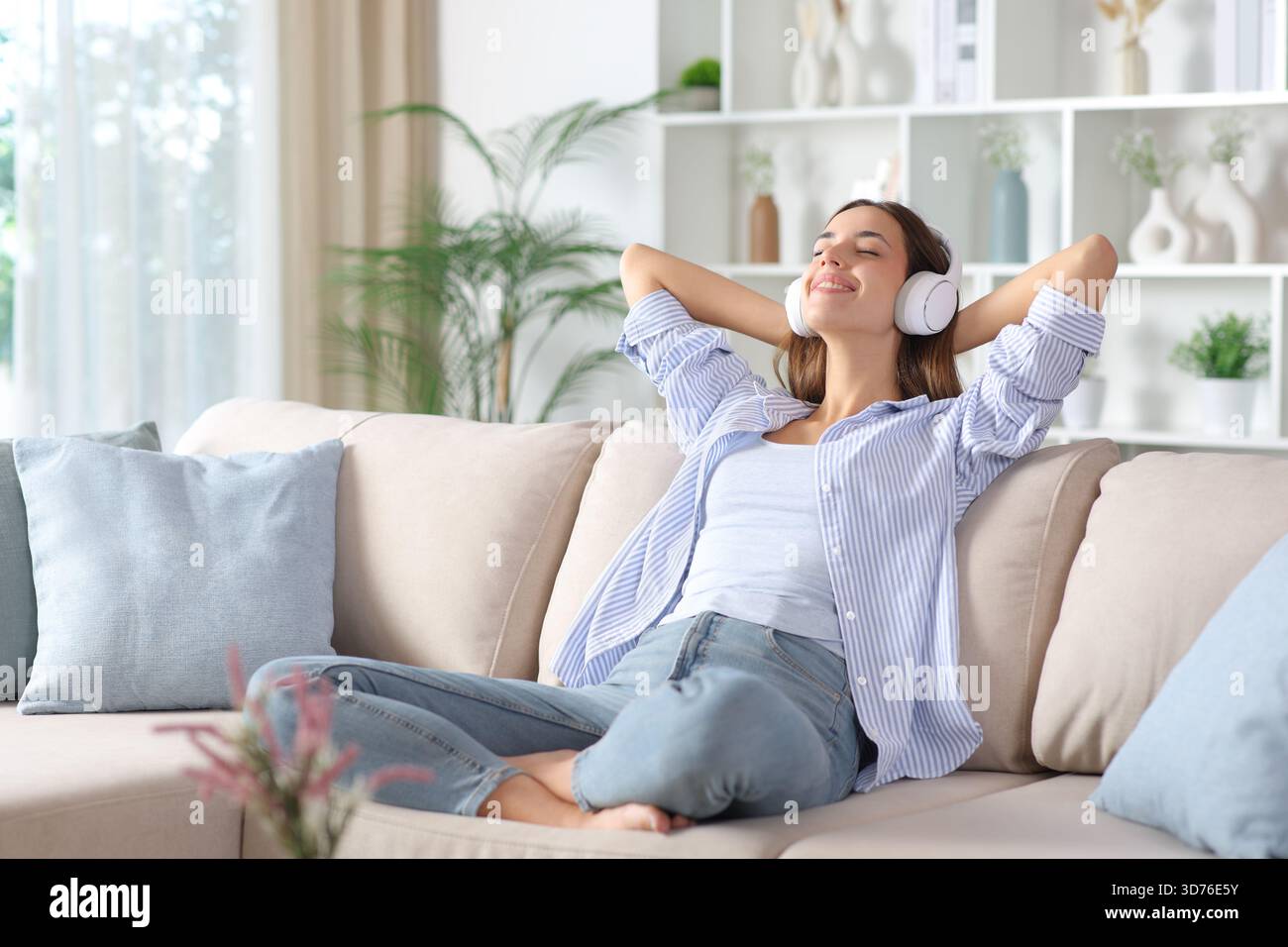 Femme heureuse portant casque relaxant assis sur un canapé à la maison Banque D'Images