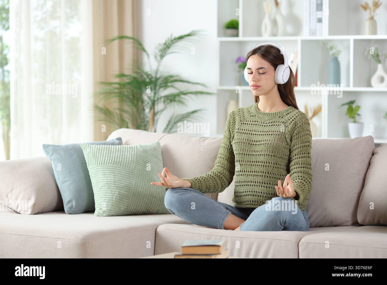 Femme en vert faisant cours de yoga guidé en utilisant un casque assis sur un canapé à la maison Banque D'Images