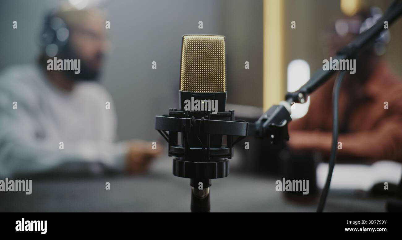 Gros plan du microphone à condensateur professionnel, fournit la technologie audio, un son de haute qualité. Deux hommes brouillaient en arrière-plan, réalisant un podcast ou une interview. Échange créatif dans l'espace médiatique moderne. Banque D'Images
