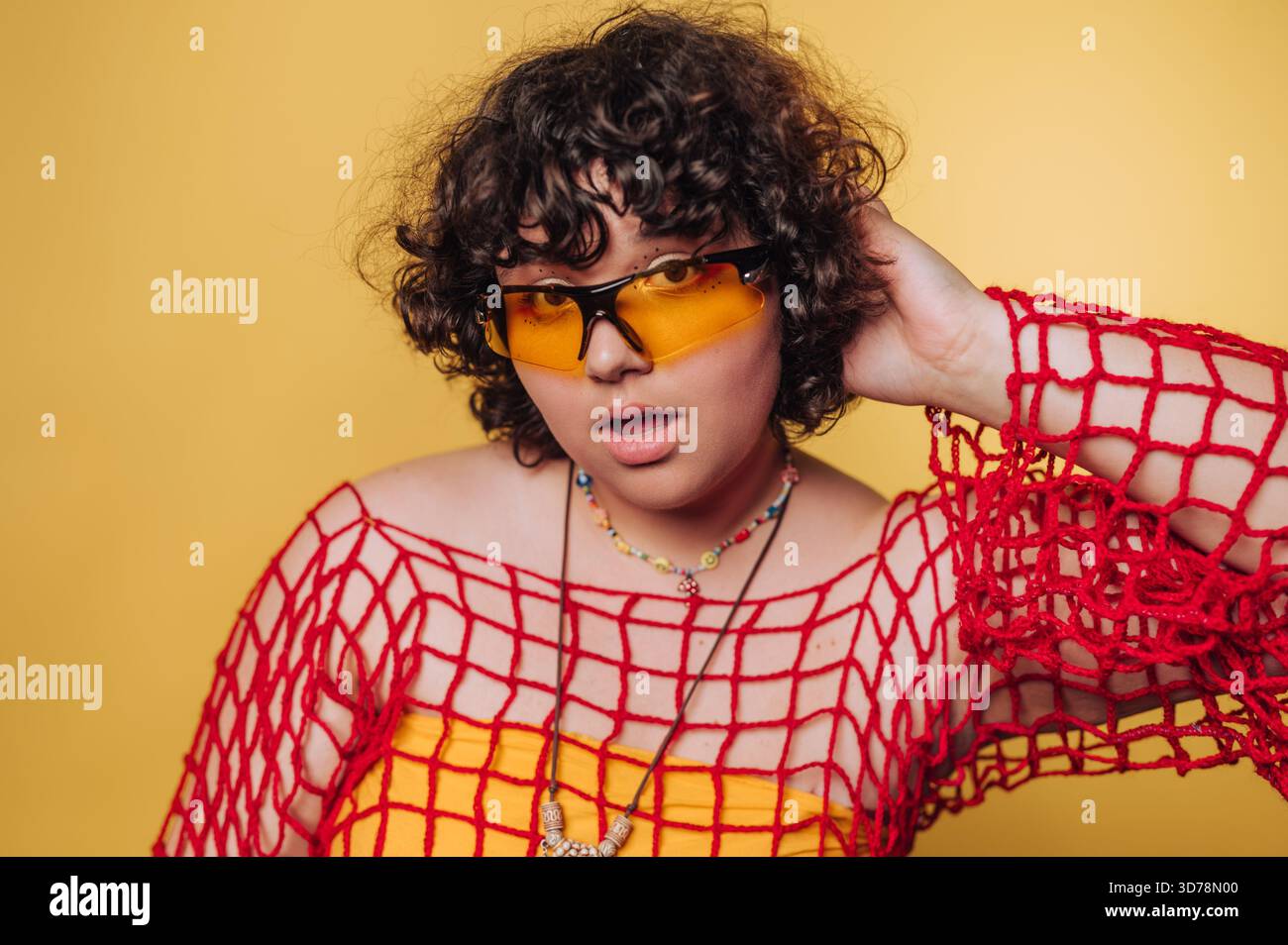 Une personne pose en toute confiance dans une tenue colorée avec un haut en filet rouge et jaune en dessous. Lunettes de soleil ajouter une touche moderne, mettant en évidence un plaisir, b Banque D'Images