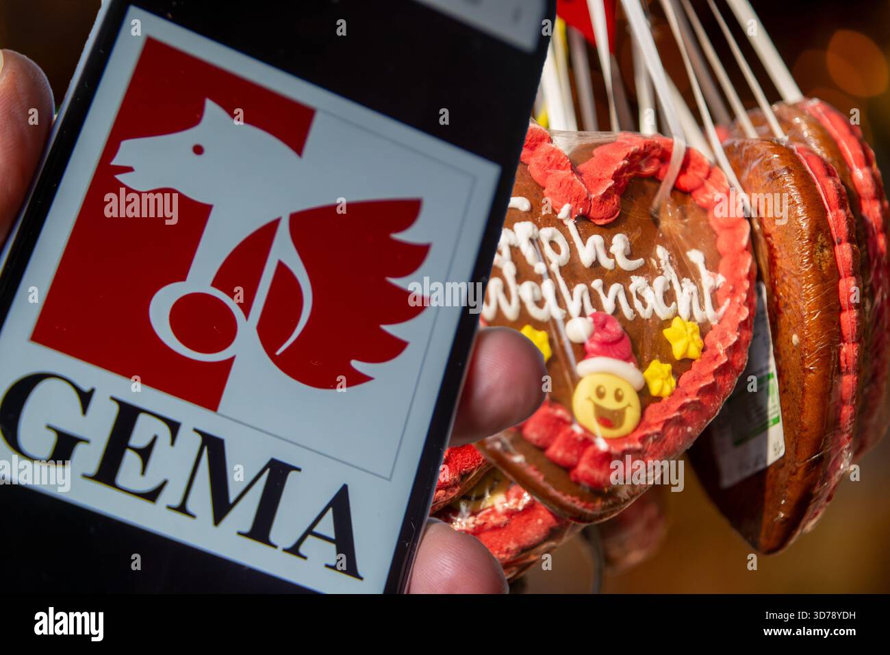 (Montage photo) smartphone avec logo Gema ouvert devant un étal sur un marché de Noël Banque D'Images