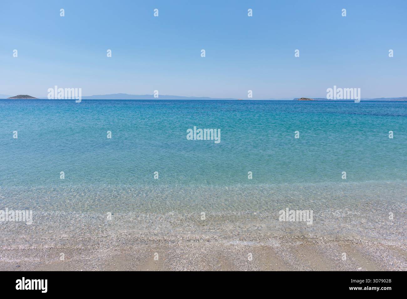 De douces vagues se glissent contre une plage de sable sous un ciel dégagé, révélant une eau cristalline Banque D'Images