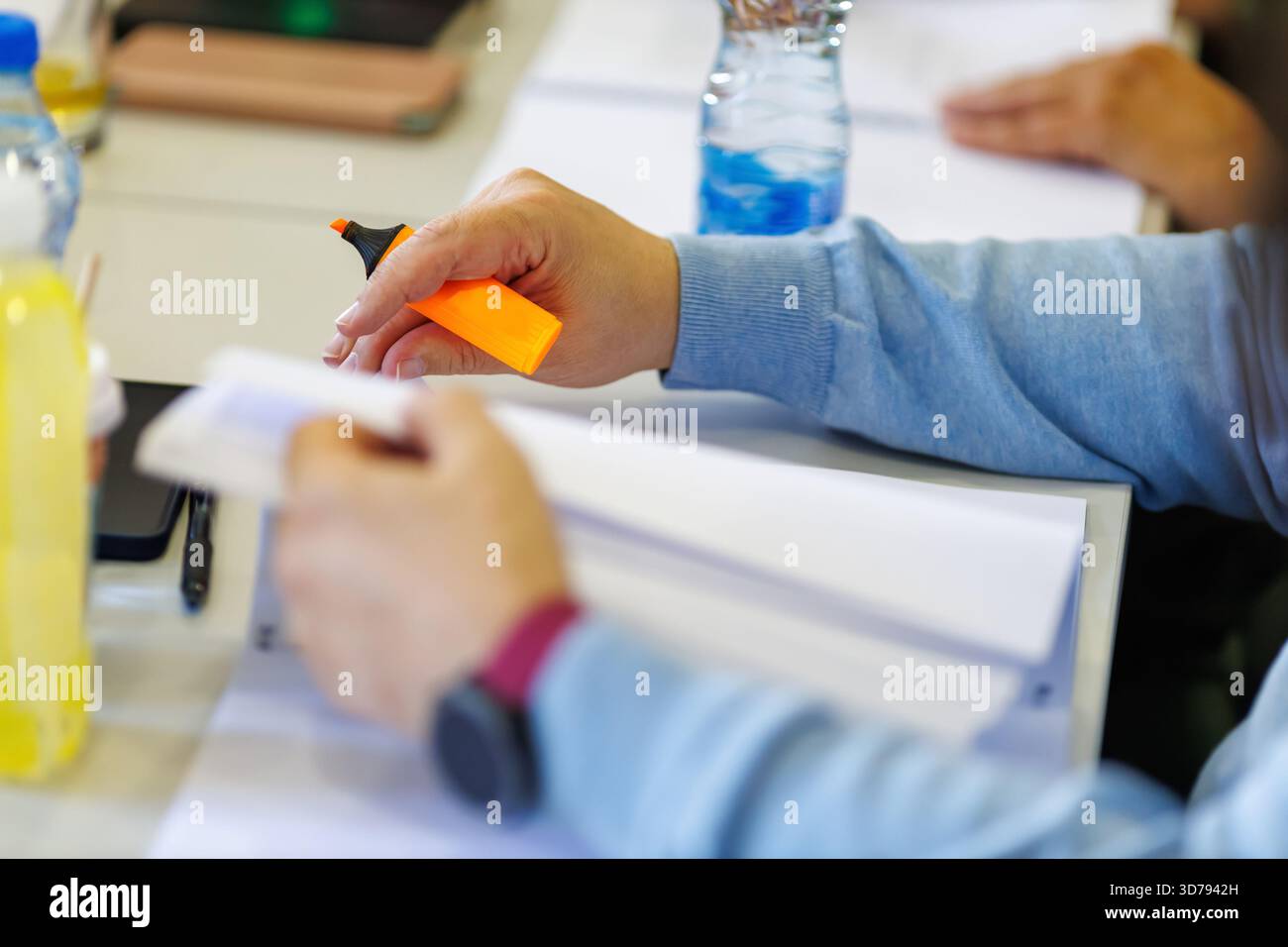 la personne souligne les notes lors d'une session d'étude à une table commune, entourée de pairs dans un environnement d'apprentissage collaboratif Banque D'Images