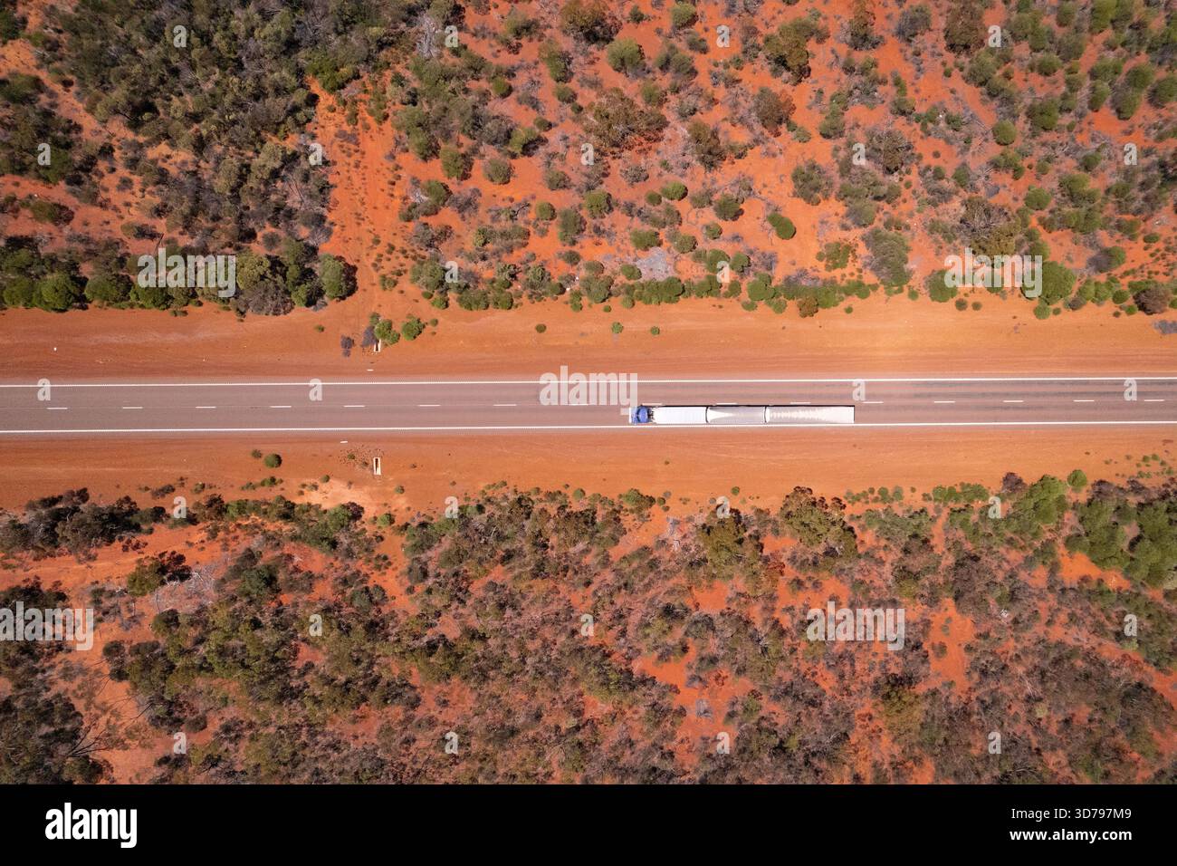 Vue aérienne d'un camion traverse une route droite coupant à travers la terre rouge et la végétation verte clairsemée, Bullabulling, Australie occidentale, Australie Banque D'Images