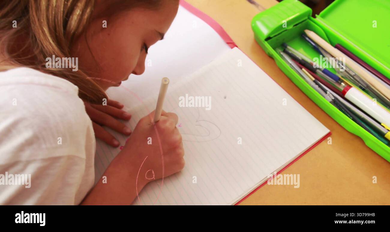 Fille chinoise penchée dans le dessin de tee-shirt blanc dans le carnet ligné au bureau, étui vert tenant un crayon pâle Banque D'Images