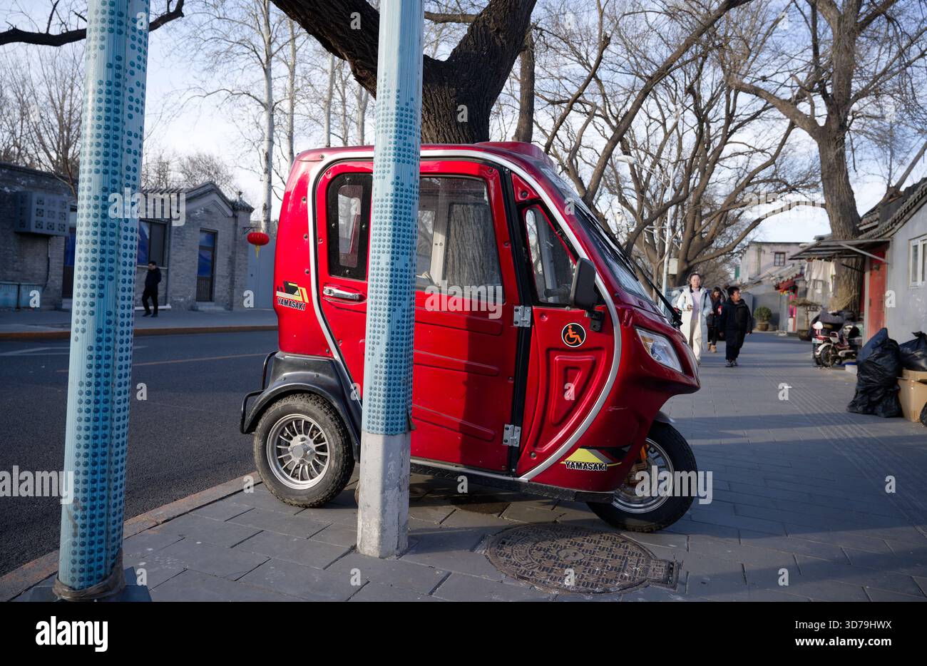 Trois-roues avec un autocollant handicapé garé à côté des poteaux sur un hutong de Pékin Banque D'Images
