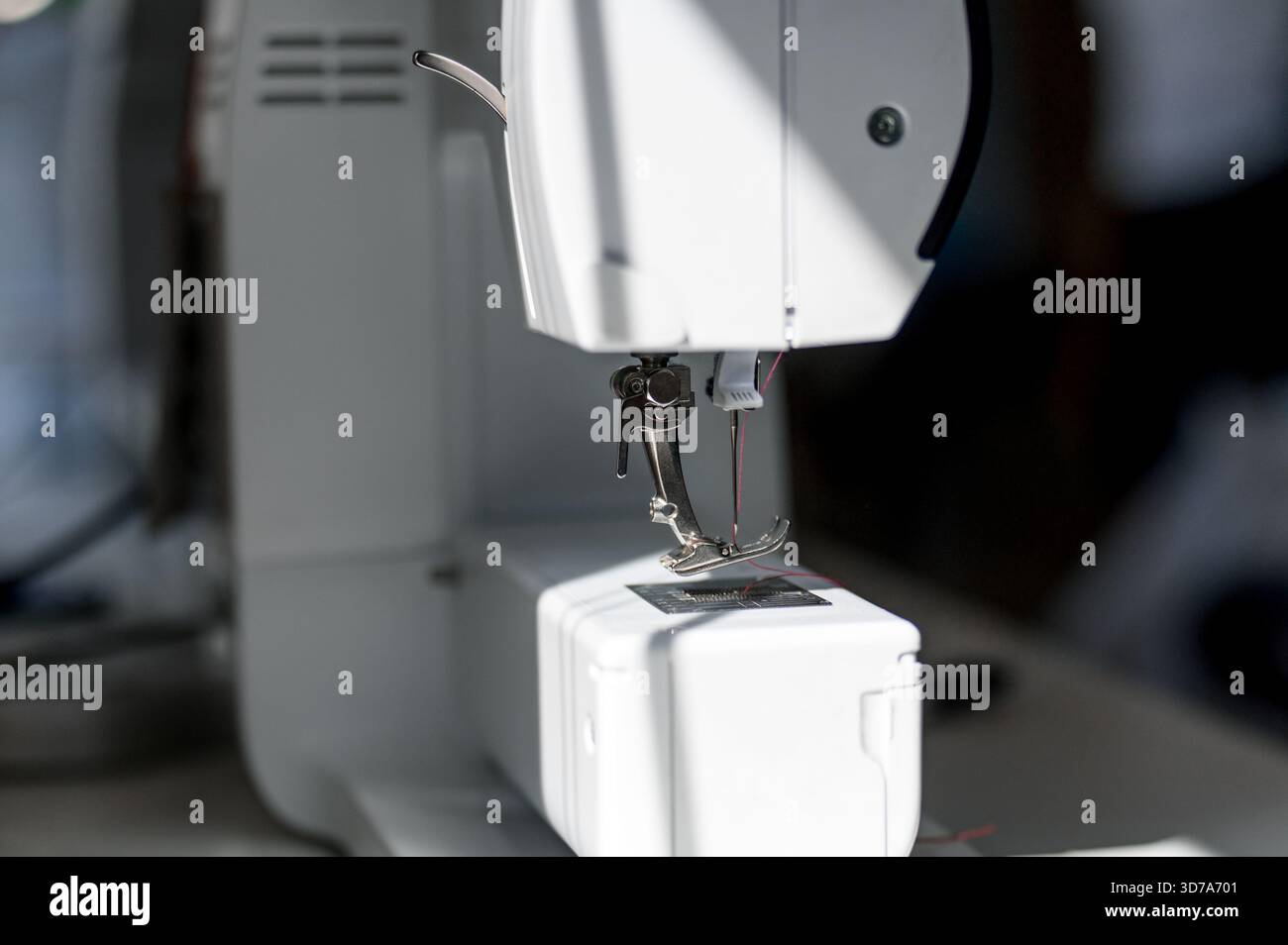 Gros plan du pied presseur et de l'aiguille d'une machine à coudre blanche moderne. Partie d'une machine à coudre domestique blanche avec un élément de travail en métal. Banque D'Images