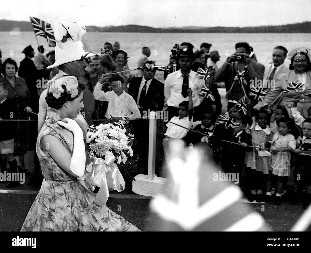 La reine aux Bermudes -- la reine marche avec le Gouverneur général des Bermudes Sir Alexander Hood à travers une file d'acclamations d'enfants peu après avoir quitté son avion à son arrivée à Kindly Field, Bermudes, le 24 novembre. Sa Majesté a passé une journée dans l'île avant de s'envoler pour la Jamaïque. À la manière de toutes les femmes, la reine vérifie les détails sur la course : l'ensemble de son col, les boucles sur son cou, l'inclinaison de son chapeau. 26 novembre 1953. (Photo d'Associated Press photo). Banque D'Images