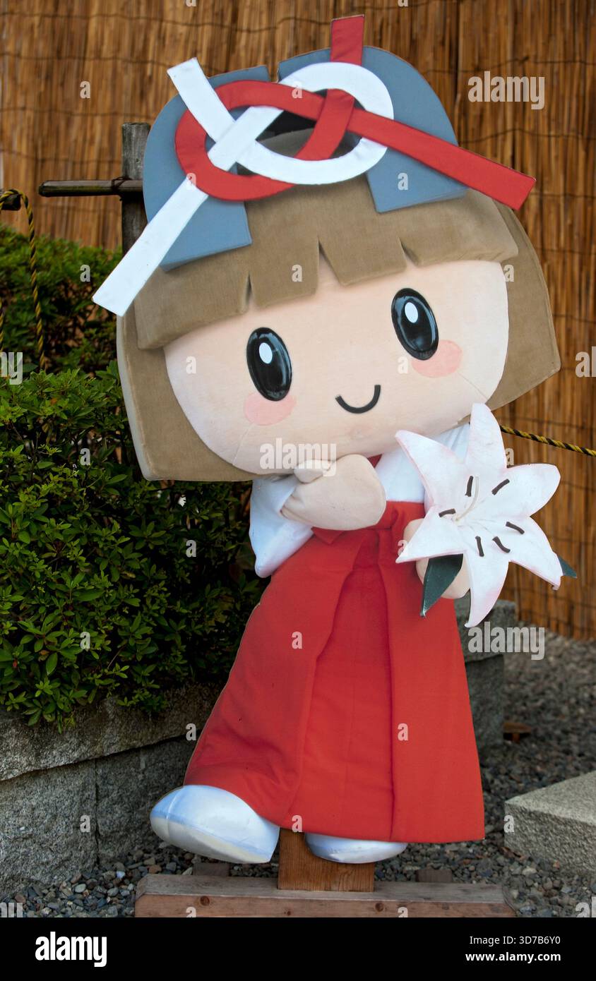 Sanctuaire Taga Taisha Shinto Yuru-kyara mascotte Tagayui-chan avec un noeud Awaji rouge et blanc 'mizuhiki' sur son chapeau portant un lis blanc, Hikone, Japon. Banque D'Images
