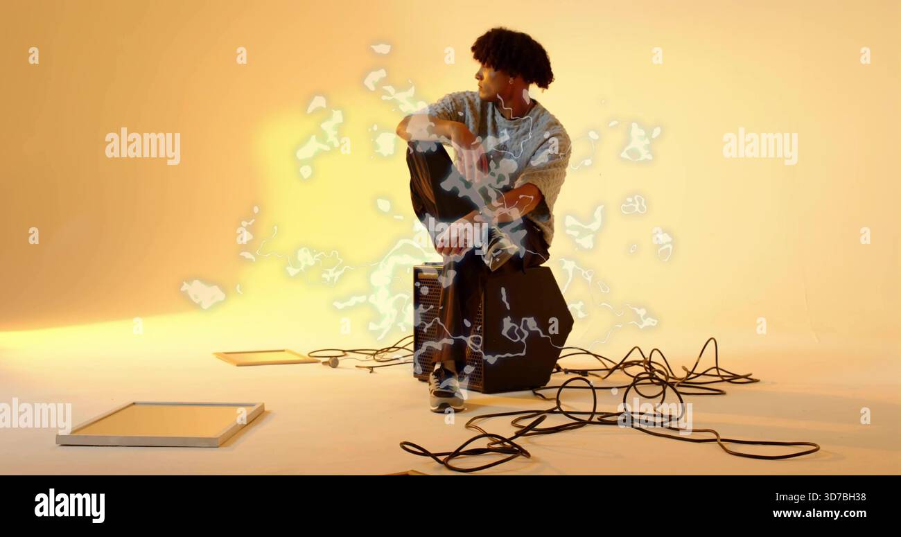 Musicien assis en pull gris écoutant avec des écouteurs dans un studio chaleureux près de l'amplificateur et des câbles Banque D'Images