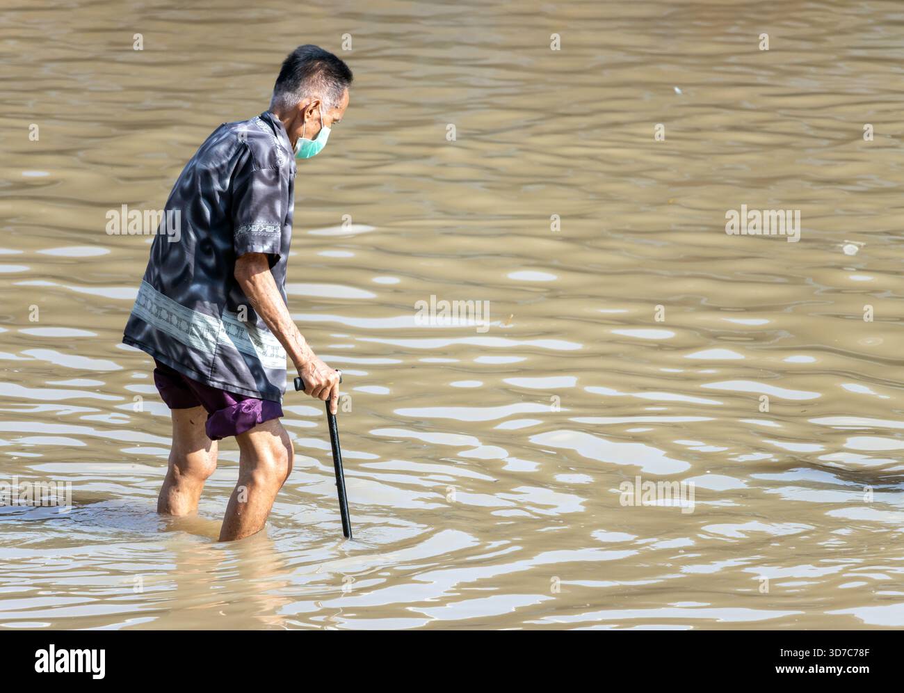 BANGKOK, THAÏLANDE, nov 09 2025, un homme âgé avec un bâton de marche patère soigneusement dans une rue inondée Banque D'Images