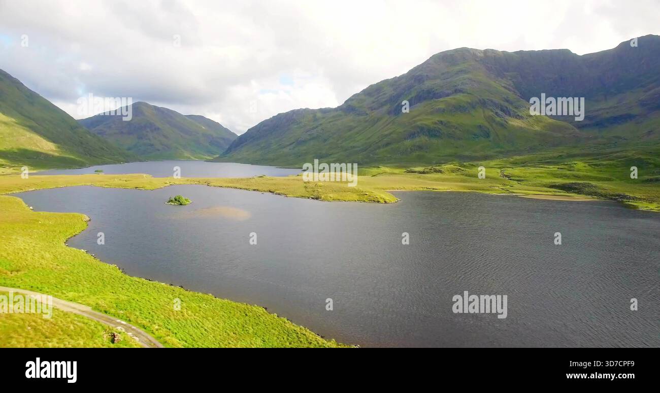 Dominant la vallée des hautes terres, grand lac d'eau douce abritant un îlot herbeux, rivage courbé et chemin Banque D'Images