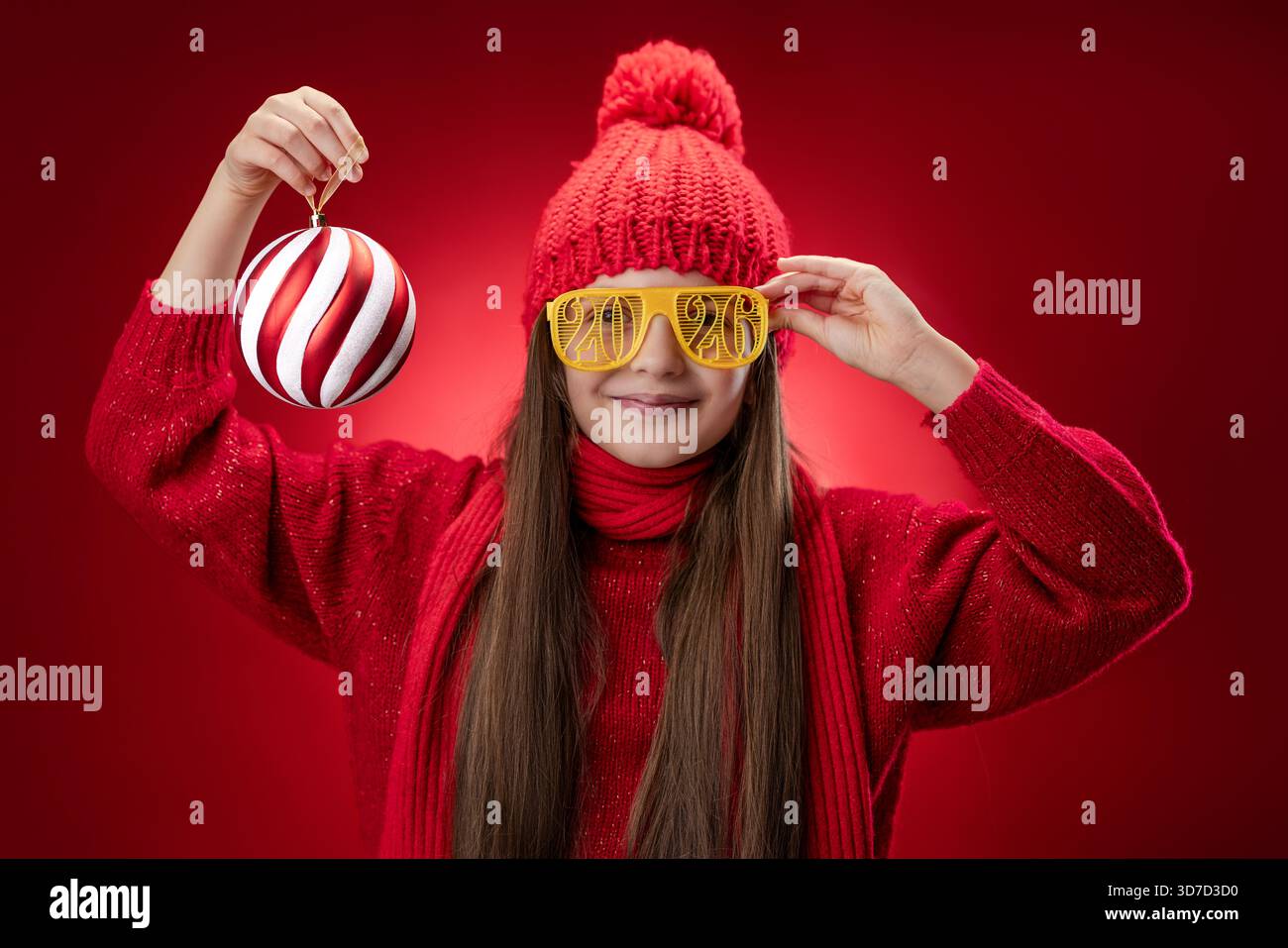 Belle femme posant avec des lunettes de soleil de noël portrait. Fille souriante avec Happy New Year 2026 lunettes de vue sur fond rouge, temps de fête pour célébrer Banque D'Images