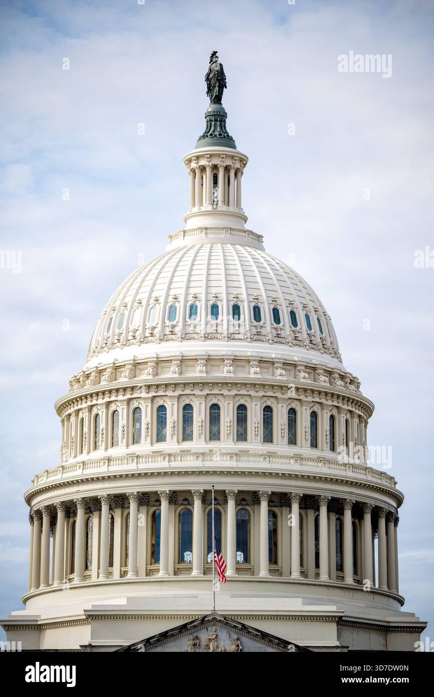 WASHINGTON DC — le dôme du Capitole des États-Unis est couronné par la Statue de la liberté en bronze. Conçu par Thomas U. Walter et achevé en 1866, le dôme en fonte s'élève à environ 87 mètres (288 pieds) jusqu'au sommet de la statue. La statue de la liberté de 5,9 mètres de haut, sculptée par Thomas Crawford, a été placée en 1863. Un drapeau américain flotte en Berne devant le dôme, signifiant le deuil national. Le Capitole est le siège législatif du gouvernement fédéral américain, abritant le Congrès américain. Banque D'Images
