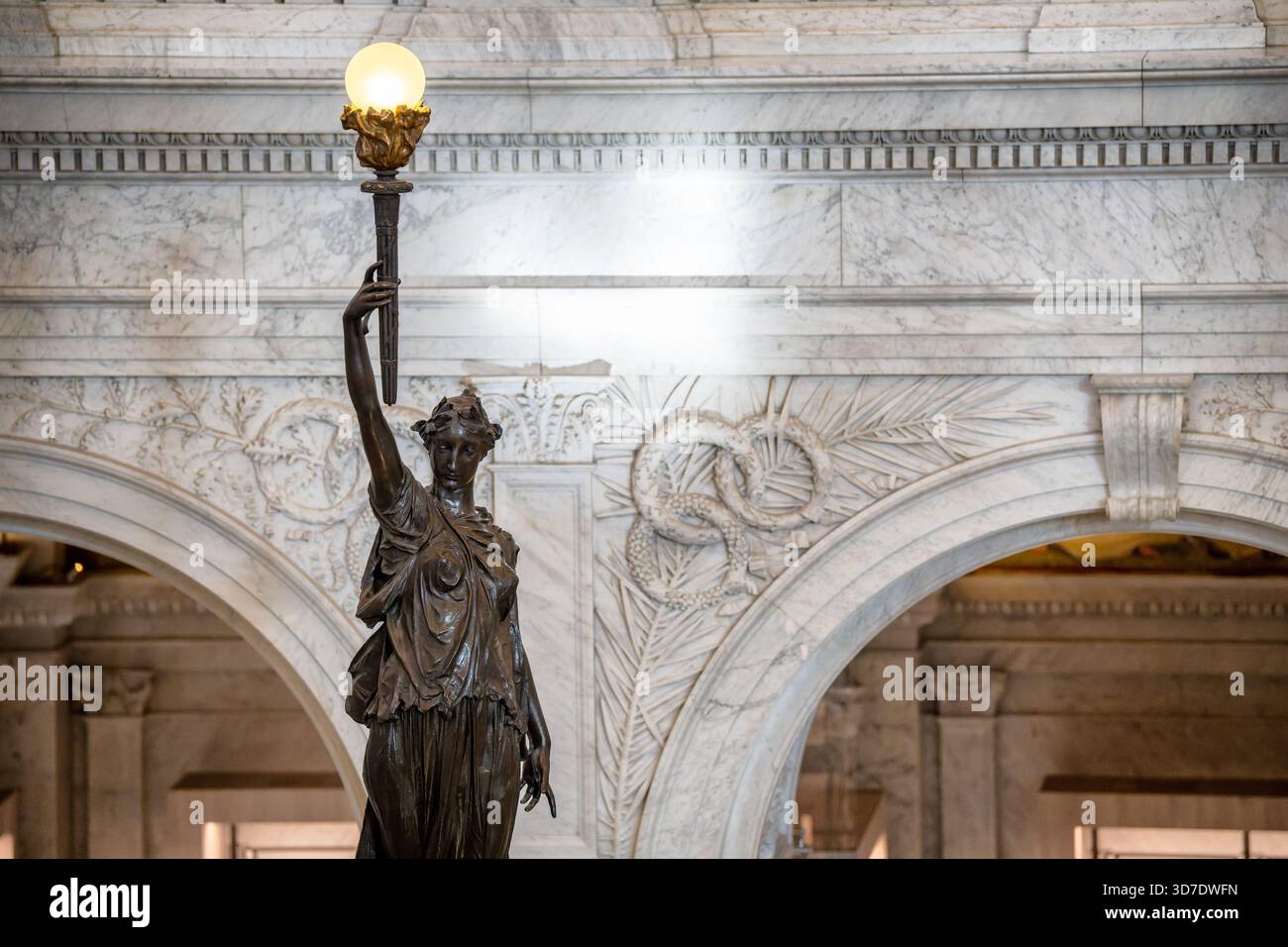 WASHINGTON DC — Une sculpture de porte-flambeau en bronze de Philip Martiny est située à la base des grands escaliers dans le Grand Hall de la Bibliothèque du Congrès Thomas Jefferson Building. Cette figure, vêtue de draperies classiques et tenant une torche de connaissance, fait partie du programme sculptural élaboré embellissant l'intérieur du bâtiment. Martiny travaille également sur des putti en marbre blanc décorant les rampes d'escalier, représentant diverses occupations et activités de la vie moderne, comme musicien, médecin et astronome. Le Thomas Jefferson Building, achevé en 1897, est l'ancien Banque D'Images