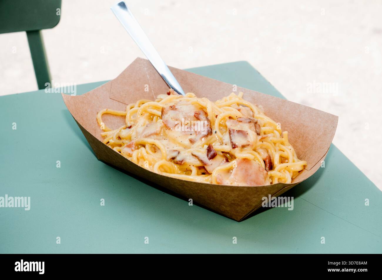 vue rapprochée de spaghetti crémeux alla carbonara avec des morceaux de pancetta servis dans un bol jetable, sur une table verte en plein air Banque D'Images