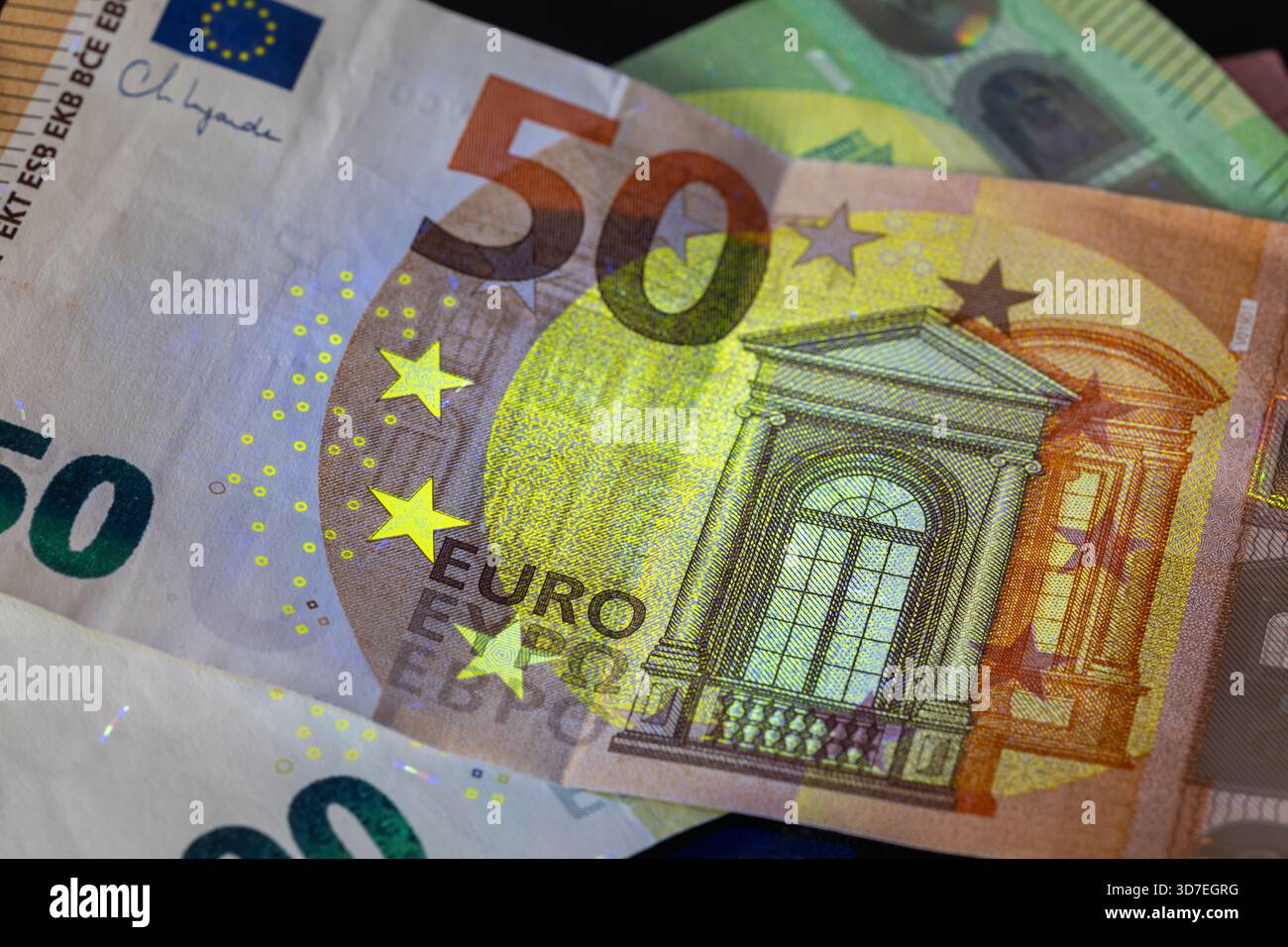 cinquante billets de banque en euros sous une puissante lumière uv, soulignant de façon spectaculaire la fenêtre architecturale, les étoiles et les caractéristiques de sécurité jaune-vert. fi européen Banque D'Images