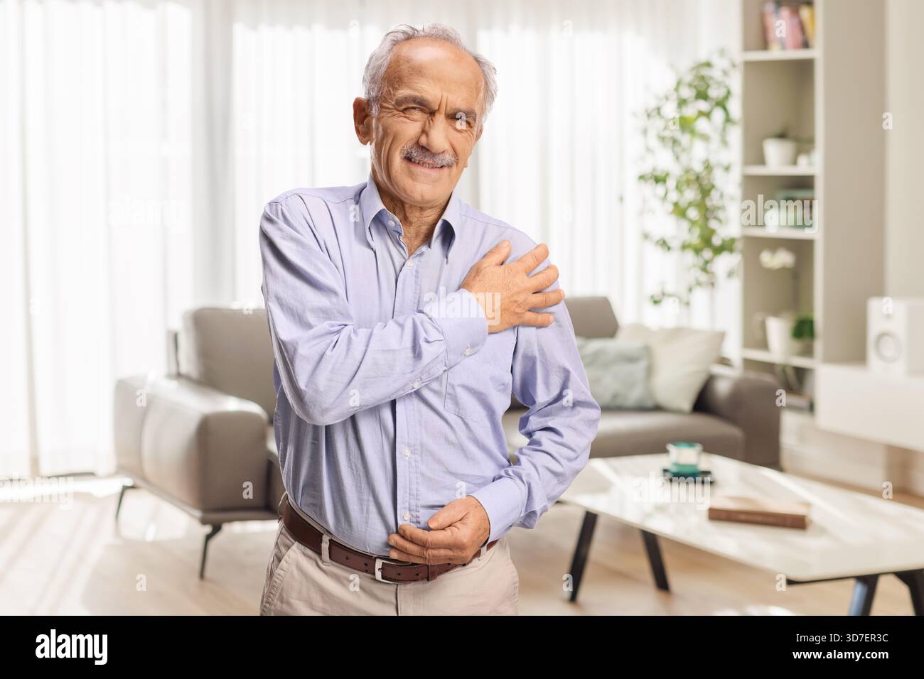 Homme âgé avec mal à l'épaule debout dans un salon Banque D'Images