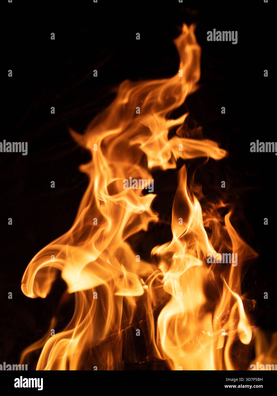 Feu capturé sur fond noir avec des languettes de flamme tordues et spirales vers le haut contre l'obscurité, créant des formes fluides qui évoquent le mouvement et le tr Banque D'Images