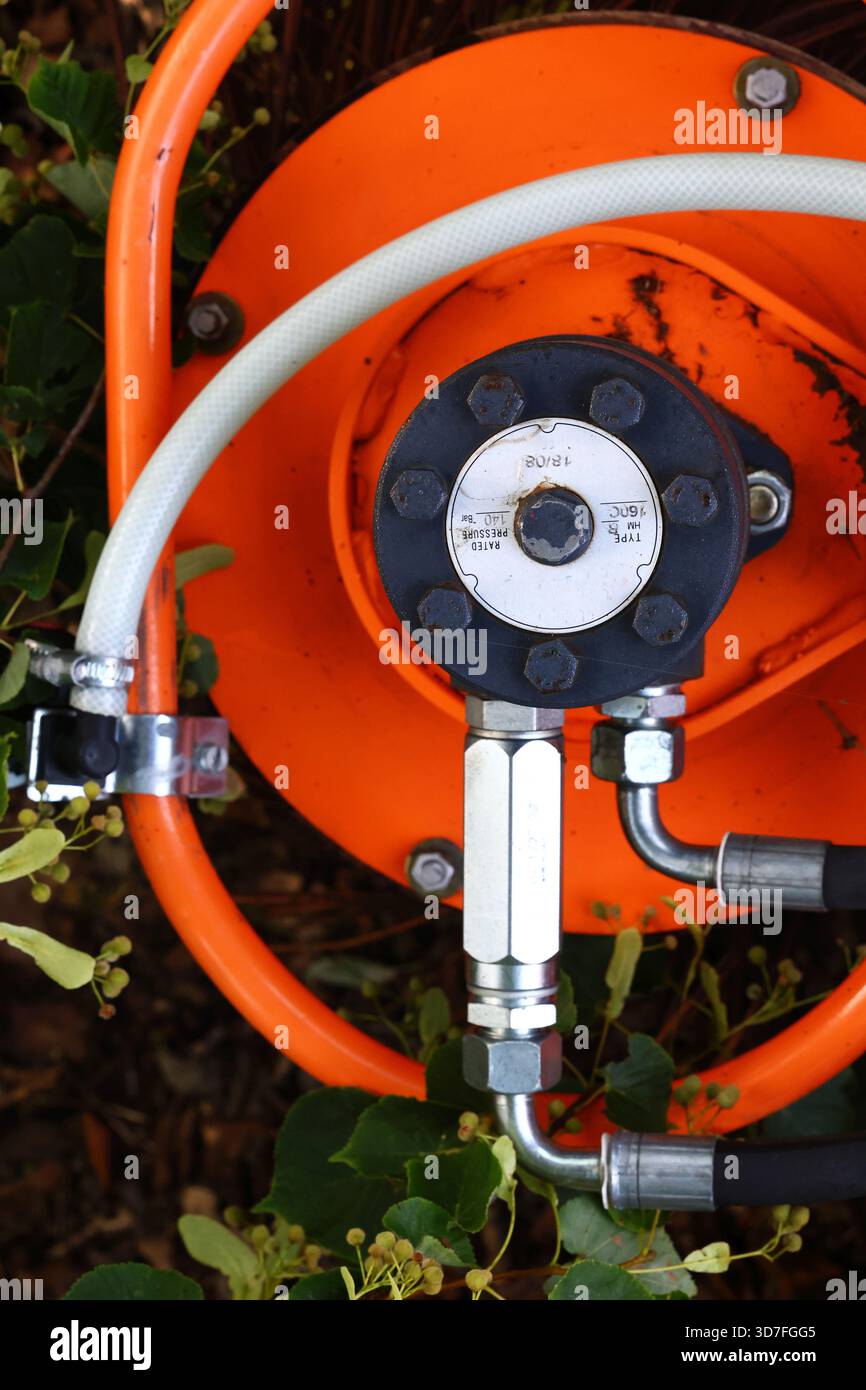 Gros plan d'un enrouleur de flexible industriel orange avec raccords hydrauliques Banque D'Images