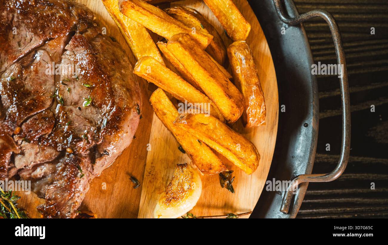 Gros plan de steak de ribeye juteux sur une planche de bois avec frites maison, tomates cerises et thym frais. Présentation gastronomique, parfaite pour le contenu alimentaire. Banque D'Images