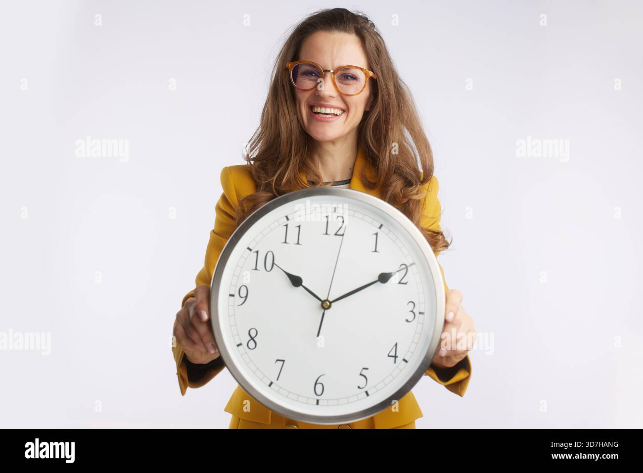 Une femme d'affaires confiante portant des lunettes tient une grande horloge analogique, représentant la précision, la conscience des délais, et la gestion efficace du temps dans Banque D'Images