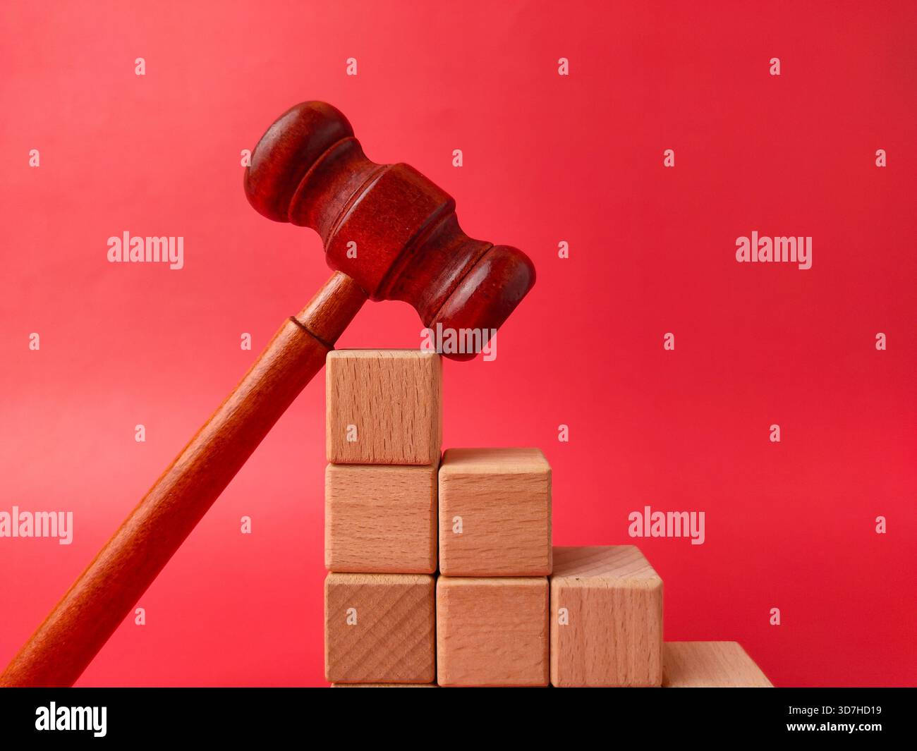 L'image montre un marteau en bois à côté d'une pile de cubes en bois sur un fond rouge. Banque D'Images
