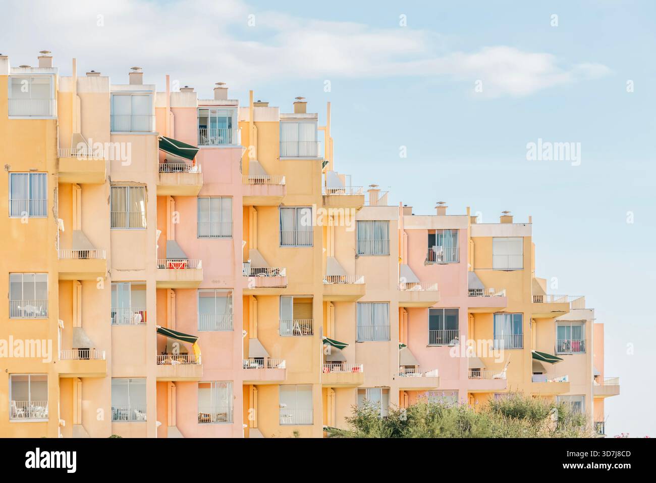 Façade courbée d'un grand immeuble d'appartement ou d'hôtel avec balcons peints dans des couleurs rose pastel et jaune sous un ciel d'été doux Banque D'Images