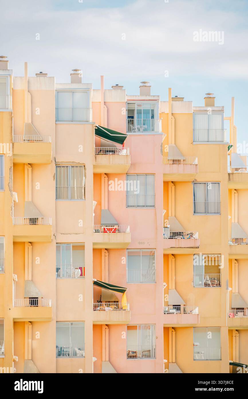 Vue verticale rapprochée du motif répétitif des fenêtres et des balcons sur un immeuble à plusieurs étages peint dans des couleurs pastel Banque D'Images