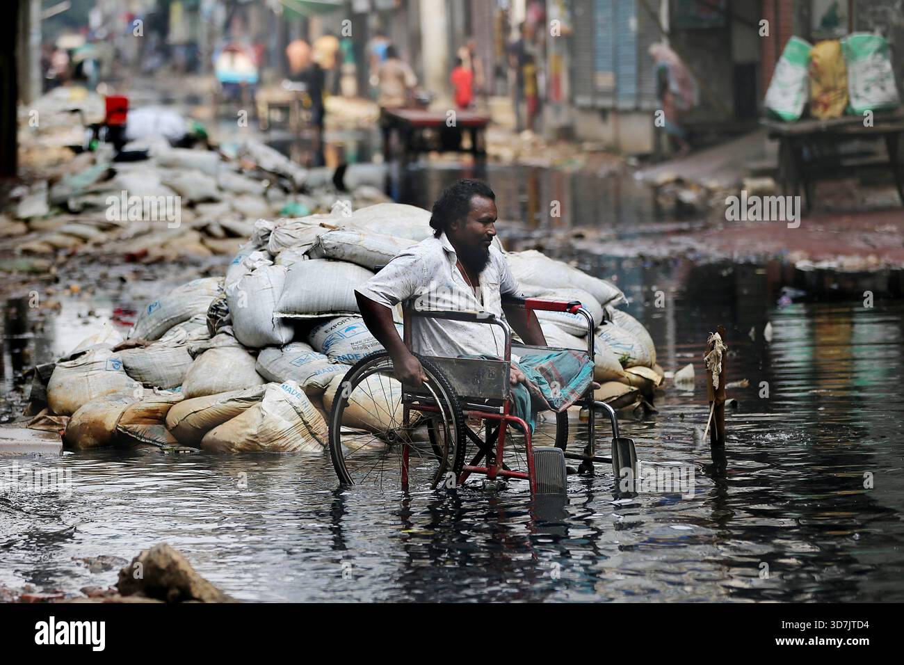 Un homme en fauteuil roulant se fraye un chemin à travers une eau noire profonde et profonde sur le Pipe Rasta de North Jurain à Dhaka. Les résidents disent que le drainage de la région Banque D'Images