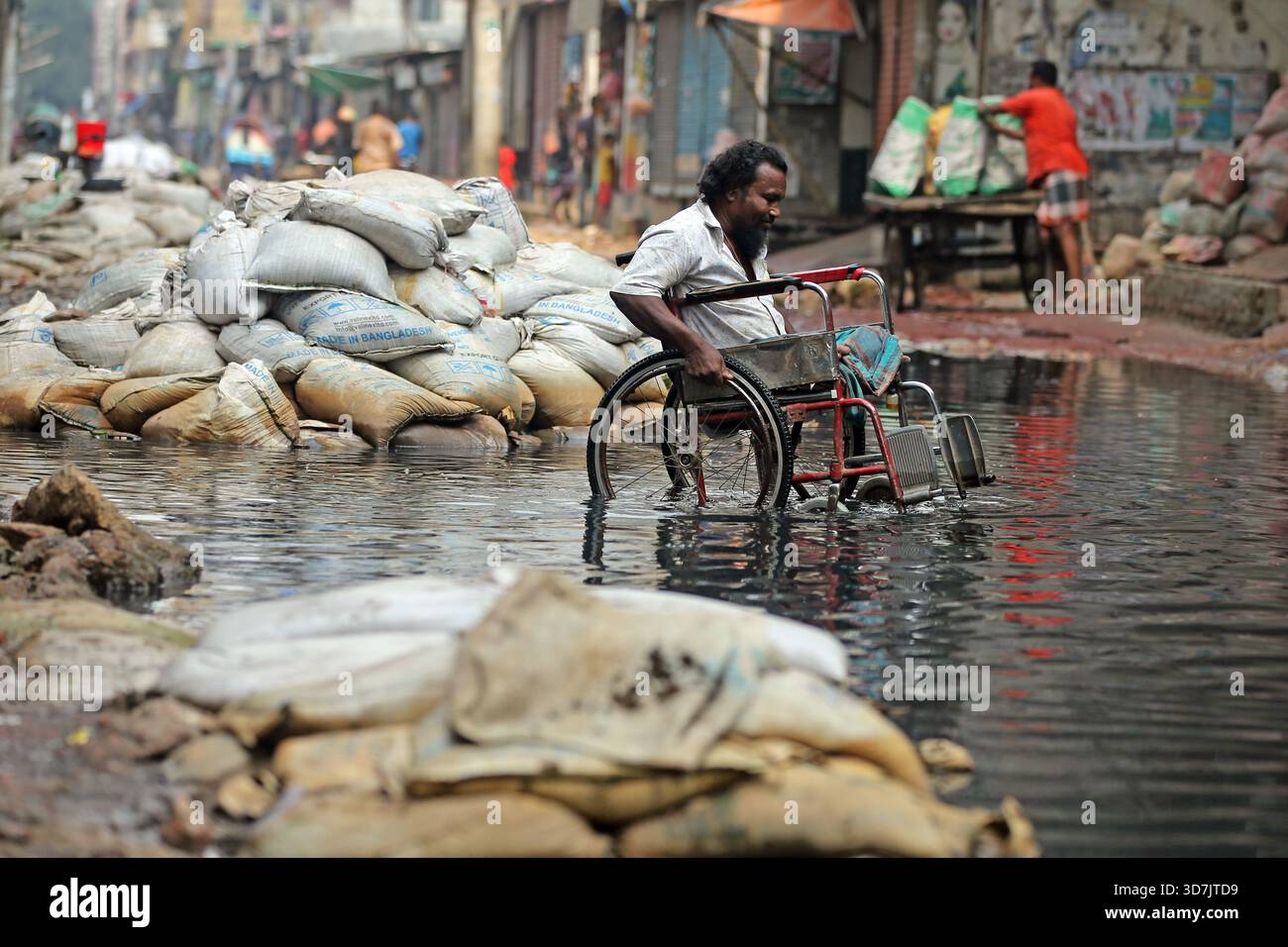Un homme en fauteuil roulant se fraye un chemin à travers une eau noire profonde et profonde sur le Pipe Rasta de North Jurain à Dhaka. Les résidents disent que le drainage de la région Banque D'Images