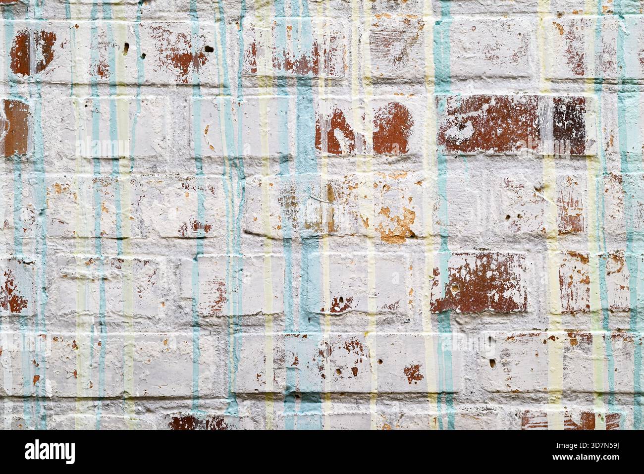 Fond de mur de briques blanches grungy avec peinture pelable et gouttes verticales de peinture bleue et jaune. Banque D'Images