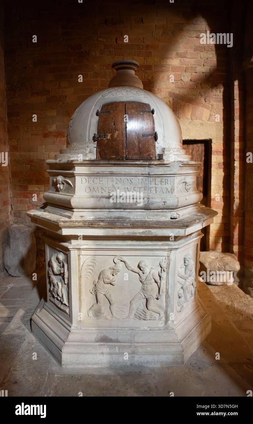 Un fonts baptismaux en pierre magnifiquement sculptée se dresse dans une lumière chaude montrant des reliefs religieux et des inscriptions latines de la tradition ancienne. Banque D'Images