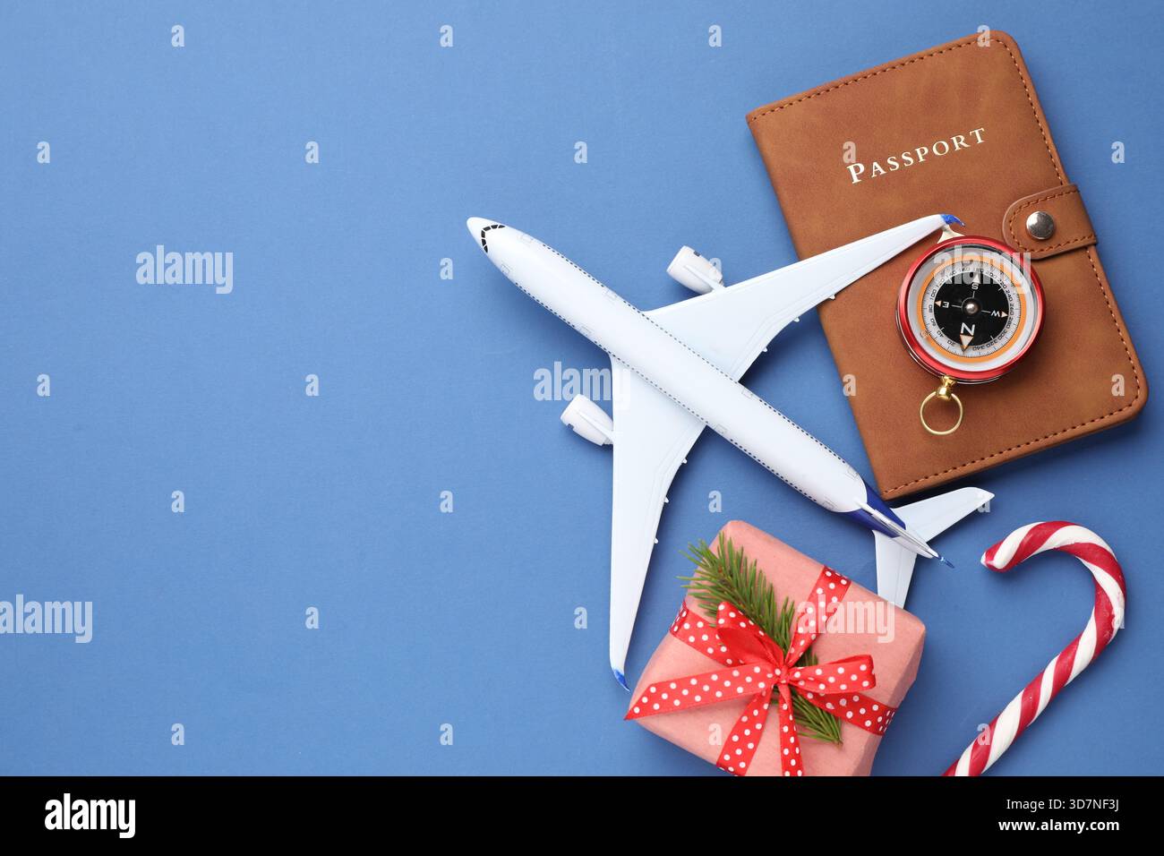 Vacances de Noël. Passeport, avion jouet, boussole, boîte cadeau et canne à bonbons sur fond bleu, plat. Espace pour le texte Banque D'Images