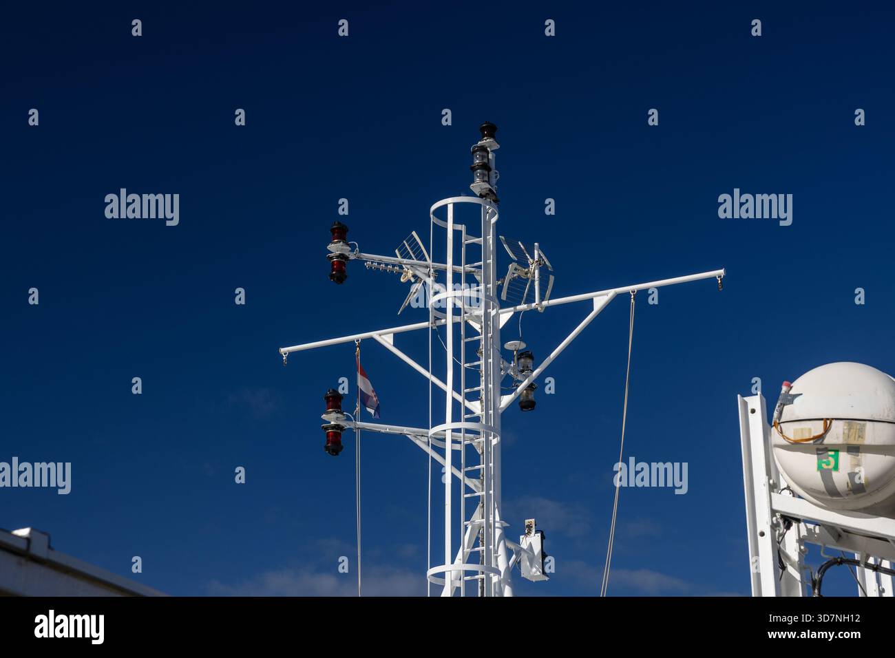 Une vue rapprochée d'un mât de navire blanc avec des feux de navigation et un gréement placé contre un ciel bleu vif, transportant la technologie nautique, la sécurité et maritim Banque D'Images