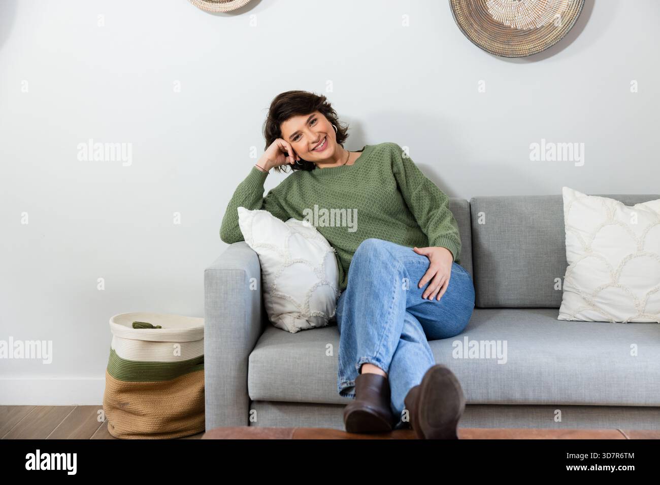 Femme appuyée sur l'oreiller blanc jeté, reposant la tête sur la main sur le canapé gris dans le salon Banque D'Images