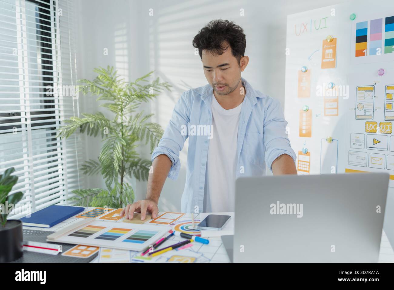 Un concepteur créatif travaille sur la planification UX/UI, analysant des croquis et des prototypes sur un tableau blanc tout en utilisant un ordinateur portable. Le processus montre la pensée de conception Banque D'Images