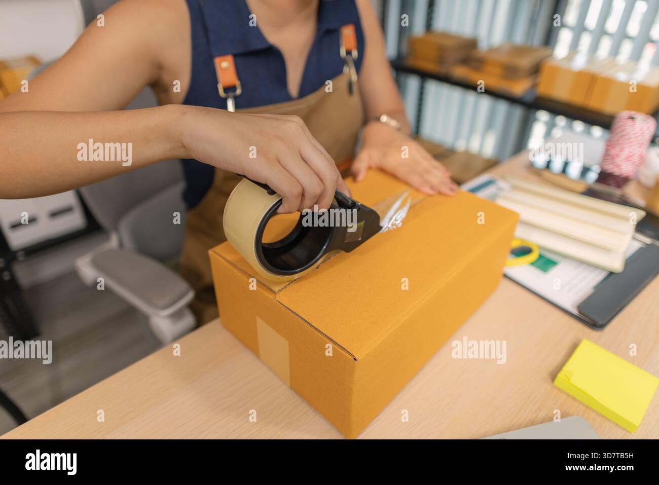 Jeune femme entrepreneure scellant soigneusement le paquet avec du ruban adhésif, préparant les commandes de marchandises, gérant l'expédition et la livraison pour son succès en ligne Banque D'Images