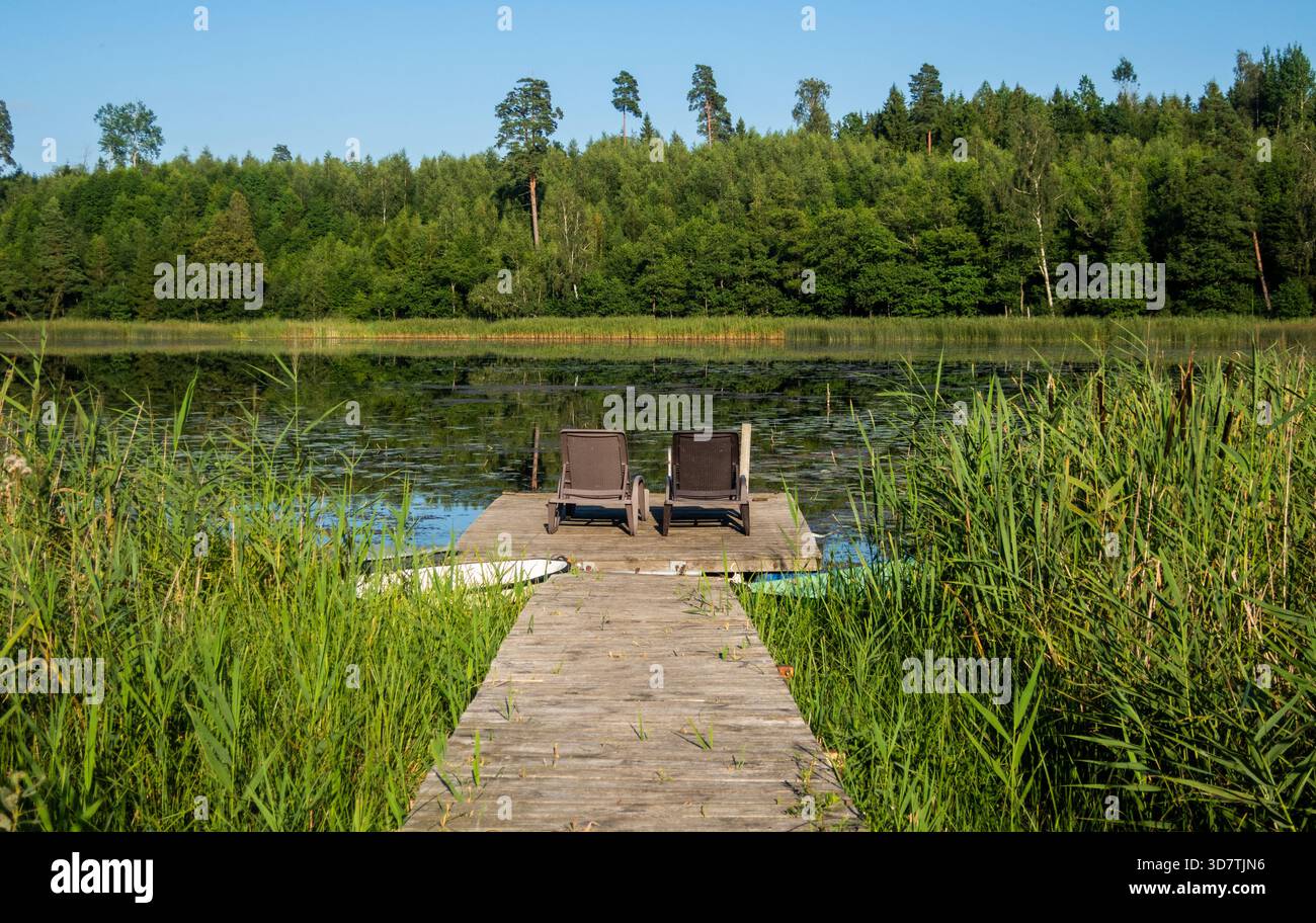 Deux chaises inclinables et des bateaux amarrés avec vue sur un lac près de Saldus dans la région de Courlande de Lettonie. Banque D'Images