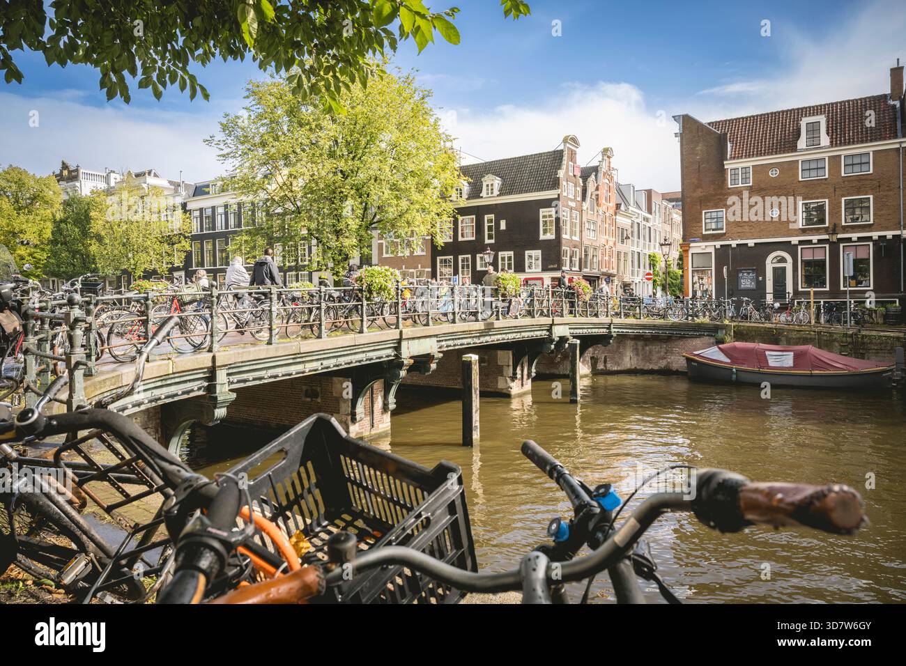 Des vélos bordent un pont de canal dans une scène de rue ensoleillée et animée d'Amsterdam avec des bâtiments historiques. Amsterdam,. Pays-Bas Banque D'Images