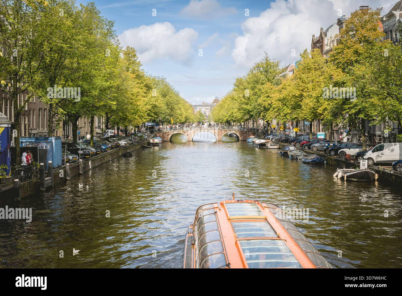 Canal à Amsterdam bordé de bateaux et d'arbres, avec un pont sous un ciel partiellement nuageux. Amsterdam,. Pays-Bas Banque D'Images